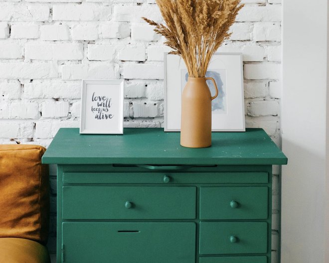 interior design picture of a decorated green dresser and a white brick wall